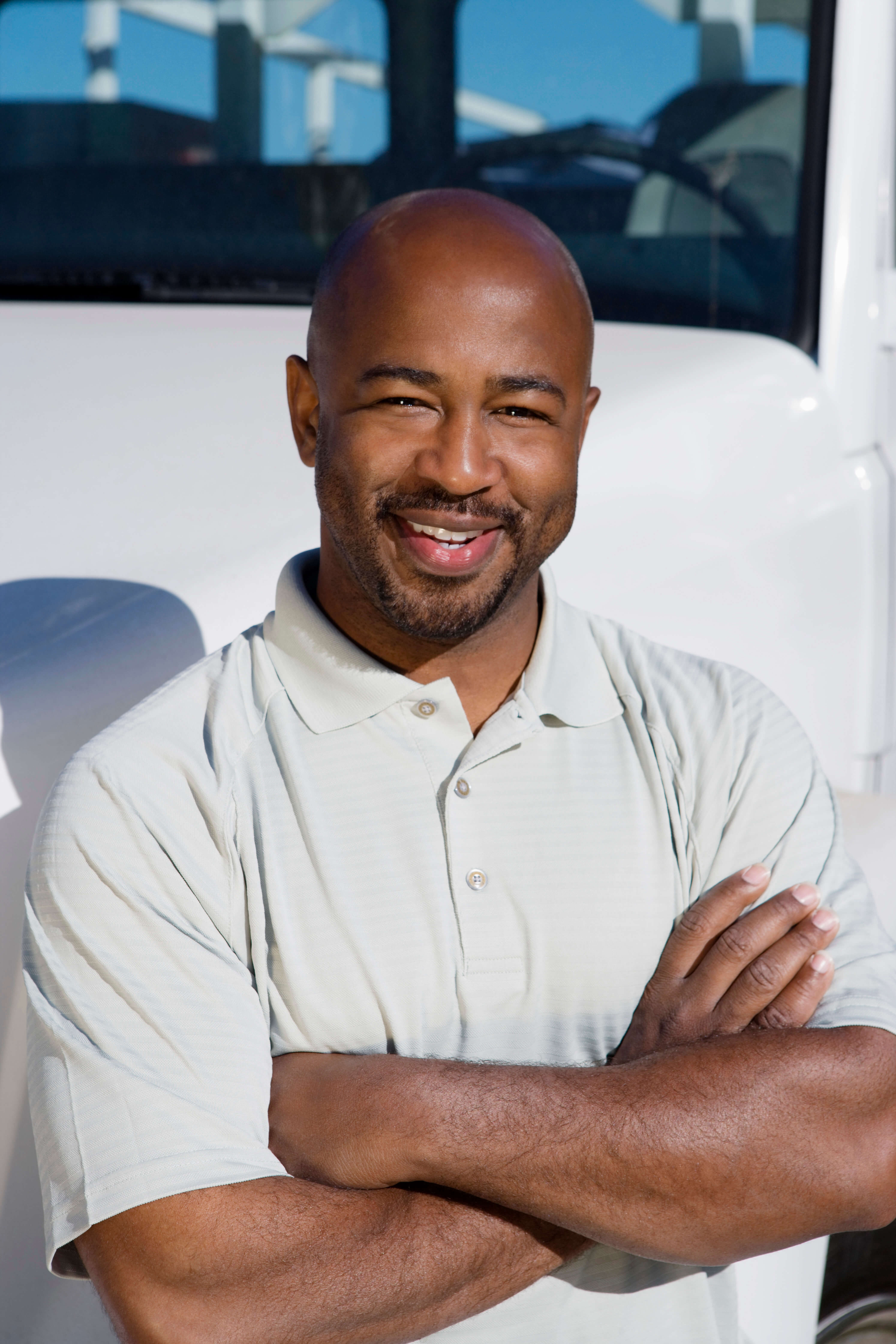 Black man stands smiling, with arms crossed on the side of a semi truck